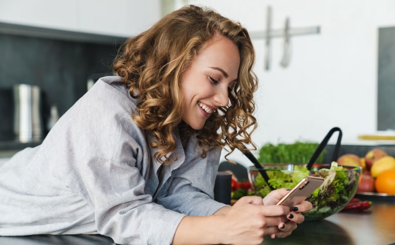 smiling-young-woman-using-smartphone-in-kitchen-3K5MASW.jpg